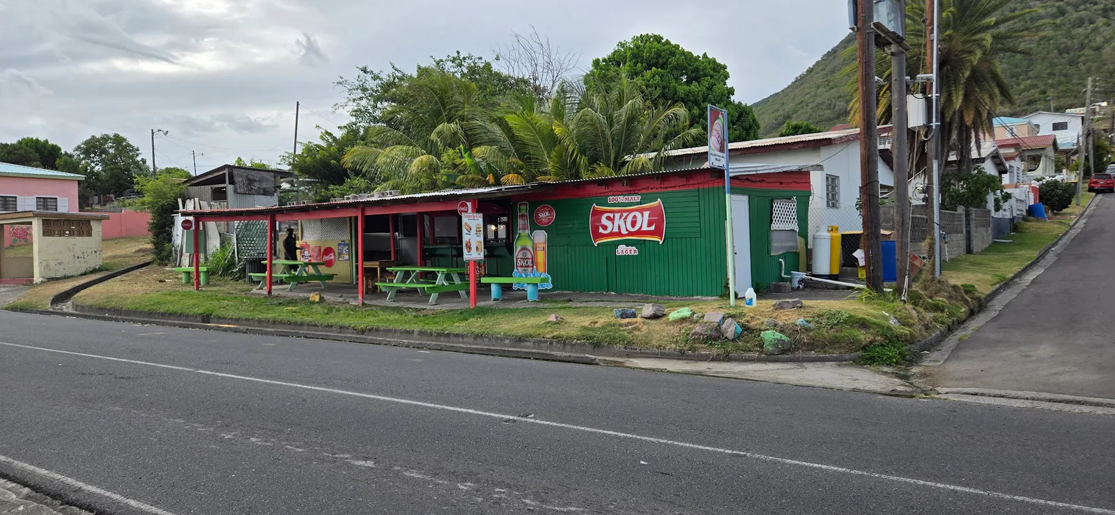 A wide street view of a green bar and neighbouring buildings along a St. Kitts road.