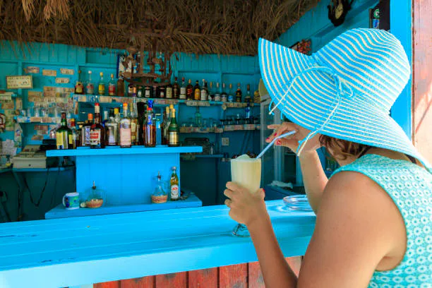 A guest in a blue sunhat holds a drink beside a bright turquoise bar.
