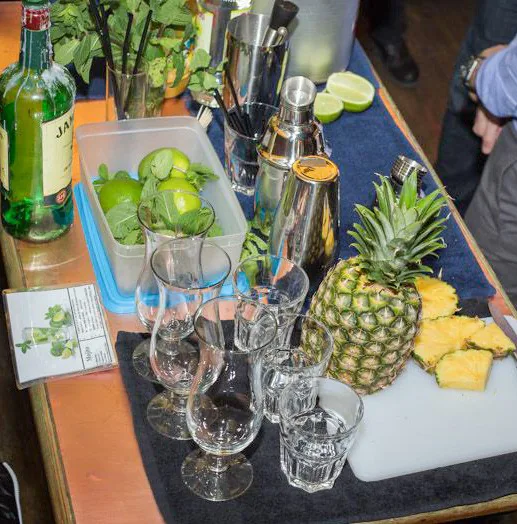 A cocktail-making station with pineapple, lime, mint, glasses and metal shakers.