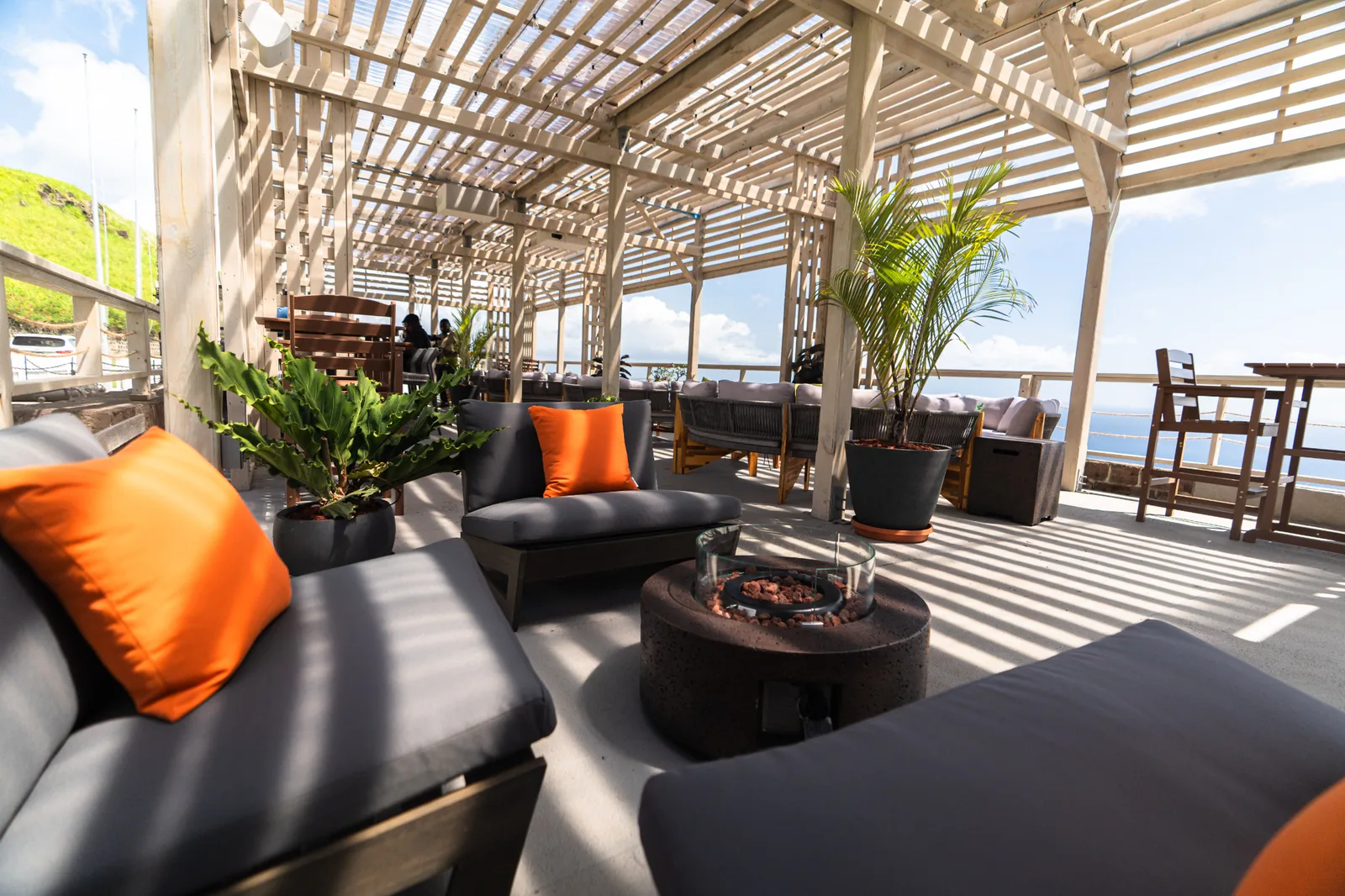 Shaded seating with orange cushions and potted palms at Gibraltar Gastrolounge, overlooking the sea.