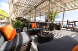 Shaded seating with orange cushions and potted palms at Gibraltar Gastrolounge, overlooking the sea.