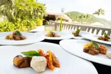 Plated food on Carambola Beach Club’s terrace with green hills and palms beyond.