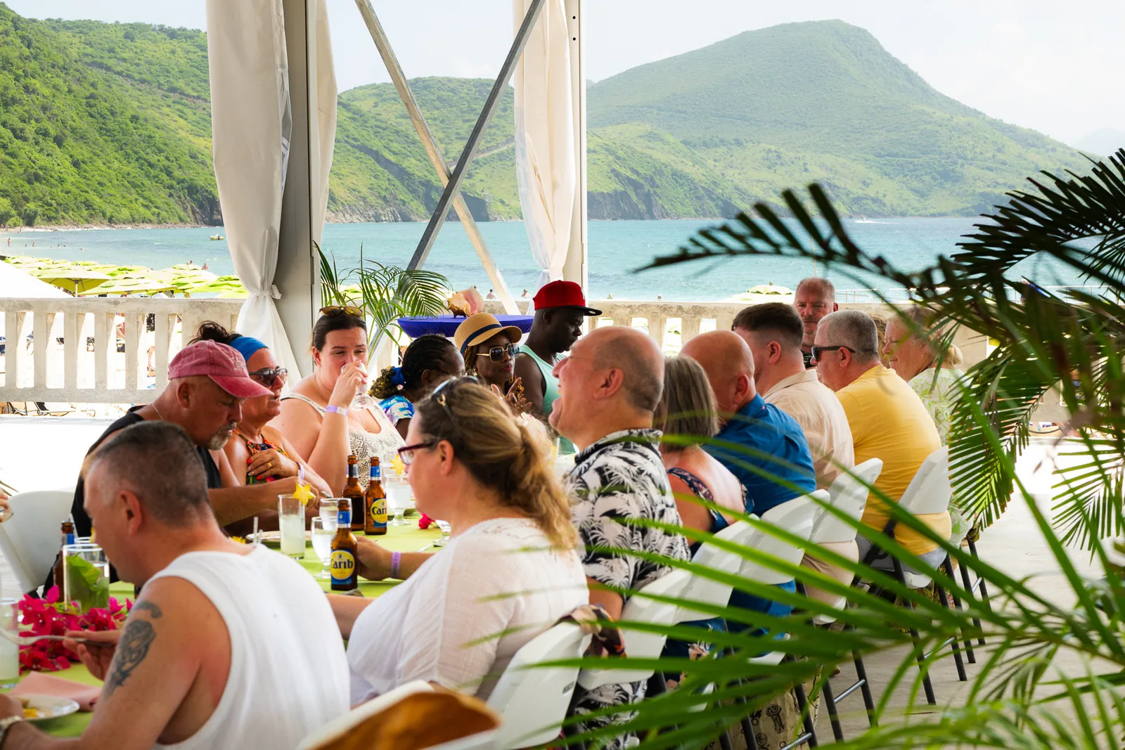 Guests dine together under a terrace canopy with St. Kitts’ green hills across the bay.