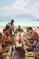Foodie tour guests enjoy their meal at a long seaside table with hills across the water.