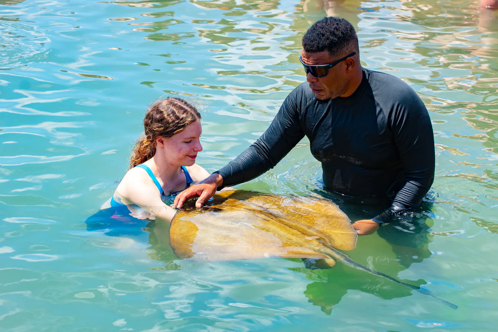 A guide helps a young guest meet a stingray in the lagoon.