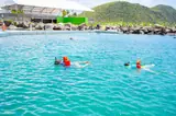 Visitors float in turquoise lagoon water with Carambola’s shoreline and hills beyond.